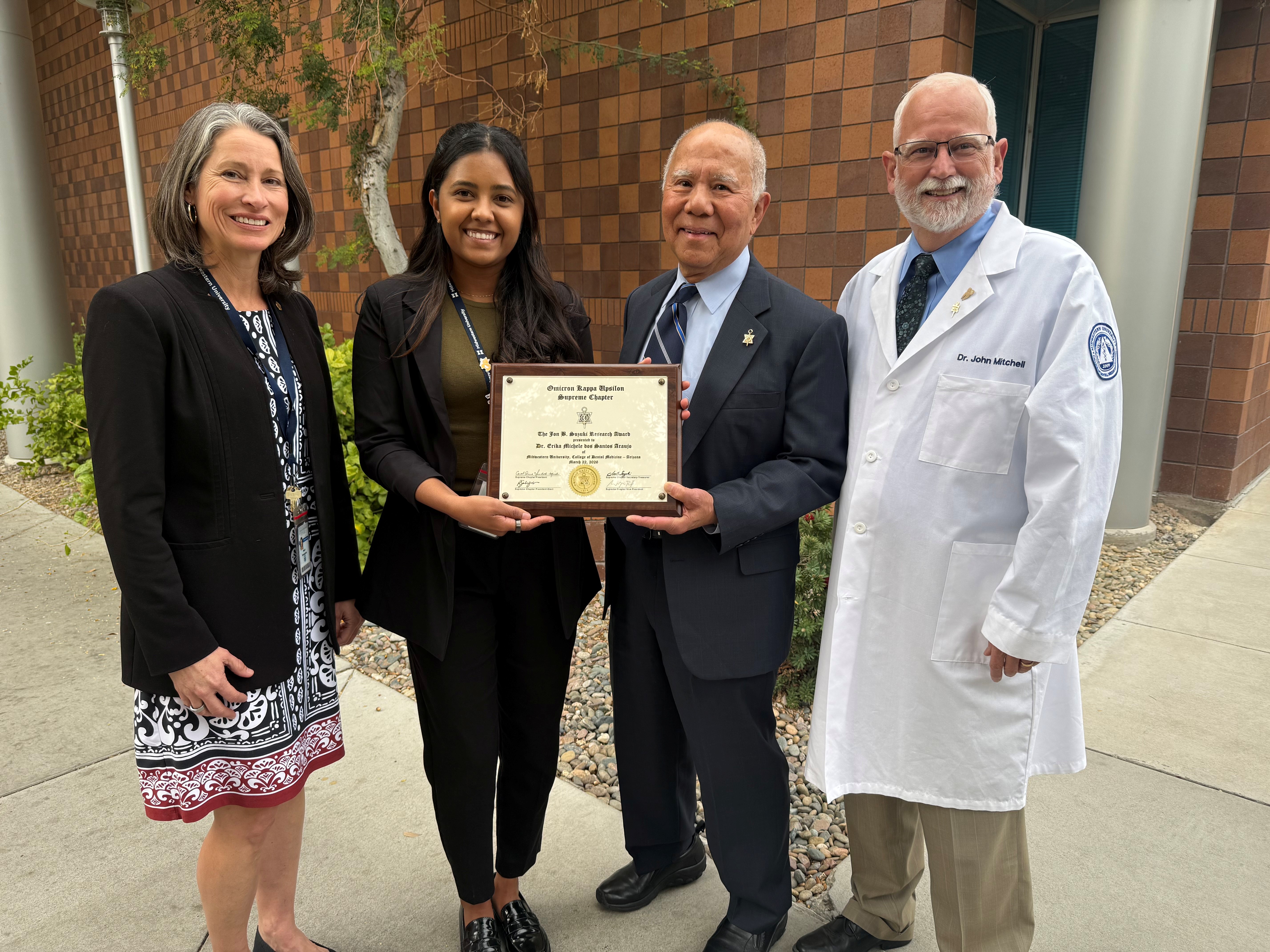 Midwestern College of Dental Medicine faculty Dr Erica Araujo is awarded the OKU Jon B Suzuki Annual Research Award. Dr Araujo is accompanied by Dean Sherri Brownstein ( left), and Associate Dean John Mitchell ( right ). The award is being presented to Dr Araujo at by Professor Jon B Suzuki at the Midwestern Campus Phoenix.